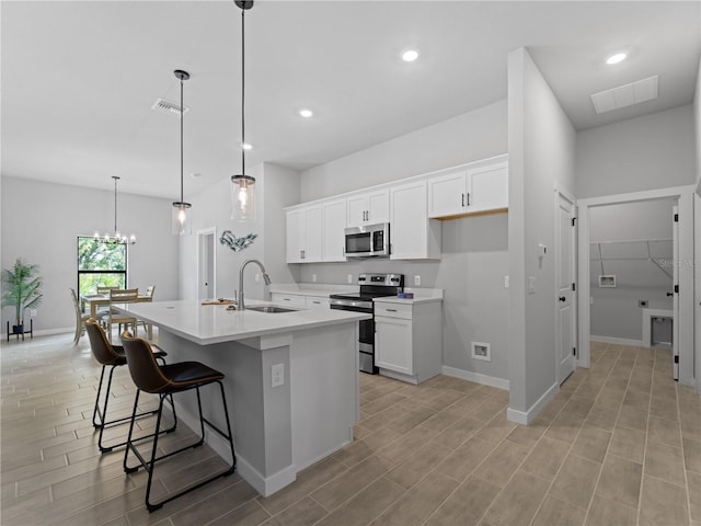 kitchen featuring sink, hanging light fixtures, stainless steel appliances, a center island with sink, and white cabinets