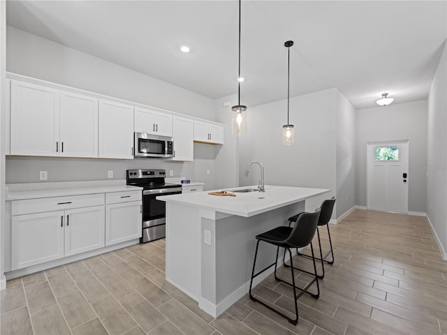 kitchen with appliances with stainless steel finishes, sink, pendant lighting, a center island with sink, and white cabinetry