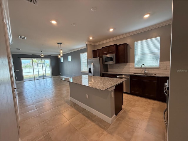 kitchen featuring ceiling fan, sink, stainless steel appliances, light stone counters, and a kitchen island