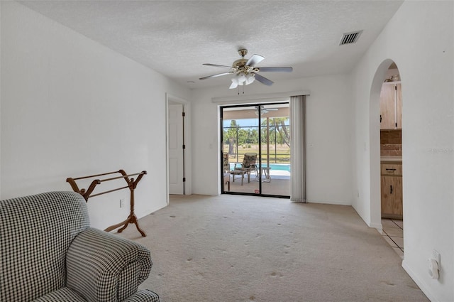 sitting room featuring light carpet, a textured ceiling, and ceiling fan