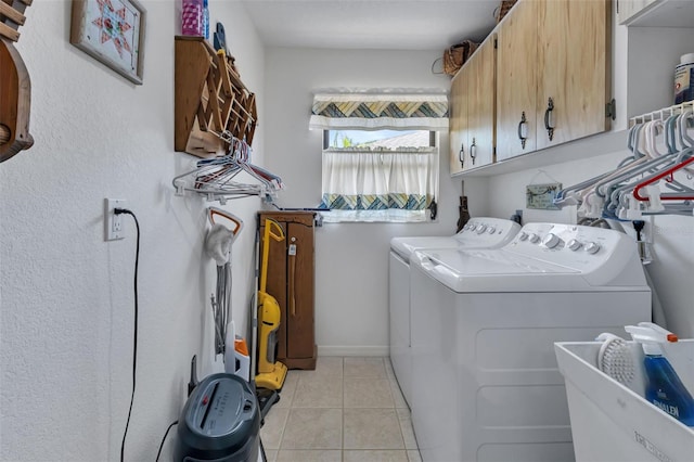 laundry area featuring washing machine and clothes dryer, light tile patterned floors, and cabinets