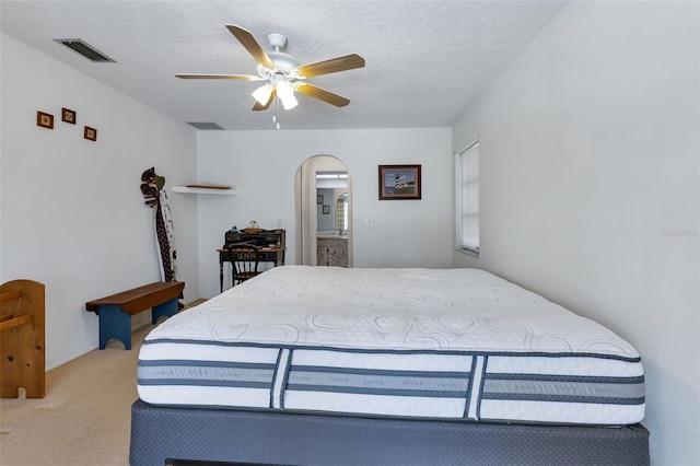 carpeted bedroom featuring a textured ceiling, ensuite bathroom, and ceiling fan