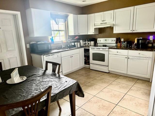 kitchen with white appliances, under cabinet range hood, white cabinetry, and light tile patterned floors