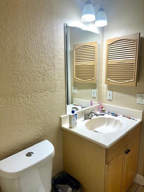 half bath with a textured wall, vanity, and toilet