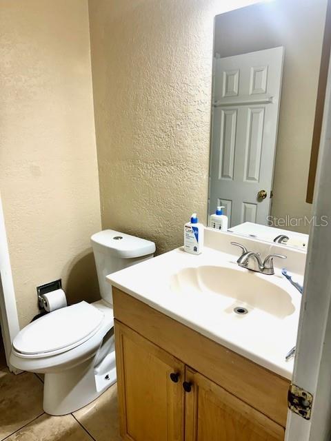 bathroom with toilet, tile patterned floors, vanity, and a textured wall