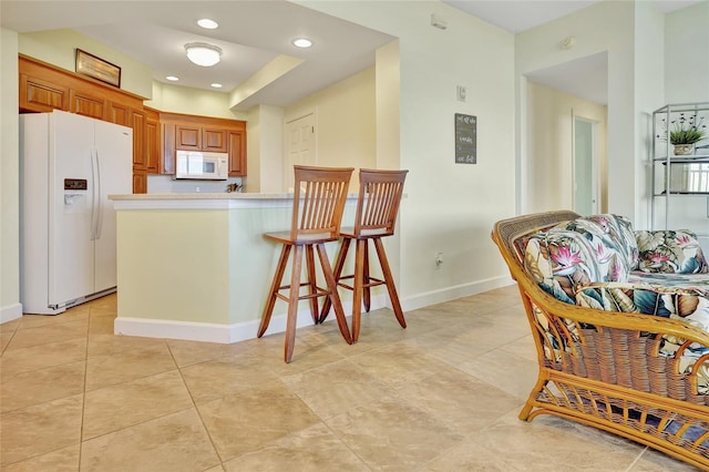 kitchen featuring a kitchen breakfast bar, kitchen peninsula, light tile patterned flooring, and white appliances