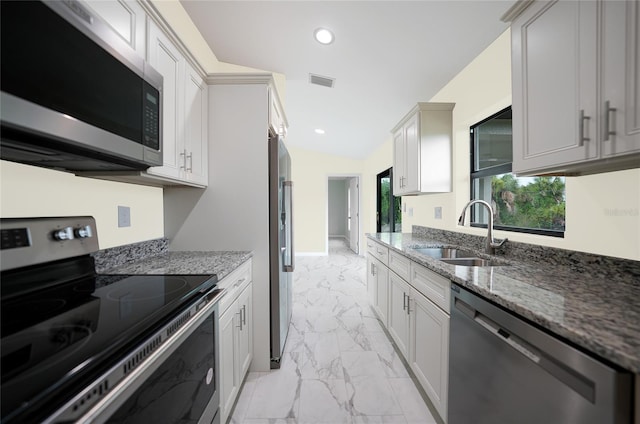 kitchen featuring stainless steel appliances, vaulted ceiling, dark stone counters, and sink