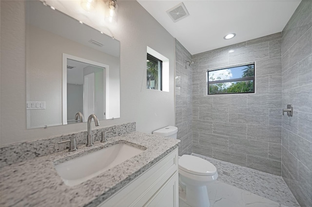 bathroom with visible vents, tiled shower, toilet, marble finish floor, and vanity