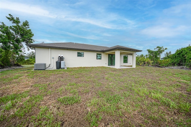 back of house with central air condition unit, a yard, and stucco siding