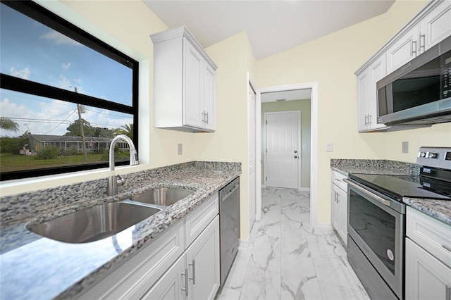 kitchen featuring lofted ceiling, sink, light stone countertops, appliances with stainless steel finishes, and white cabinetry