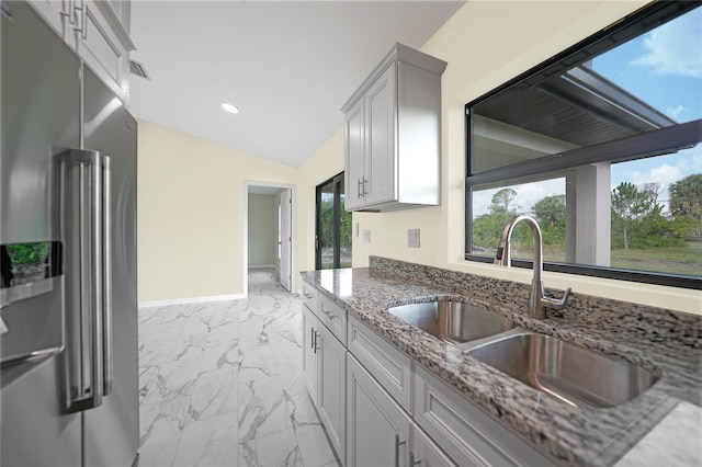 kitchen featuring high end refrigerator, sink, light stone countertops, and vaulted ceiling