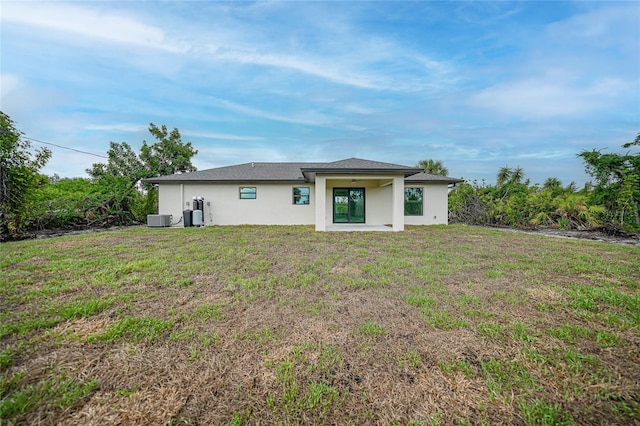 back of house featuring central AC unit, a lawn, and stucco siding