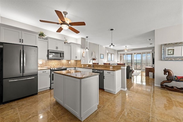 kitchen featuring stainless steel appliances, kitchen peninsula, dark stone countertops, decorative light fixtures, and a kitchen island