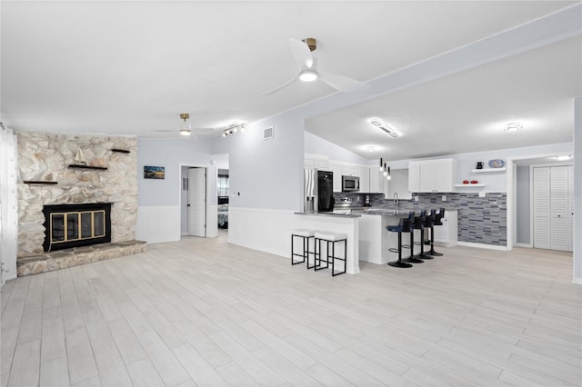 tiled living room featuring a stone fireplace, ceiling fan, lofted ceiling, and sink