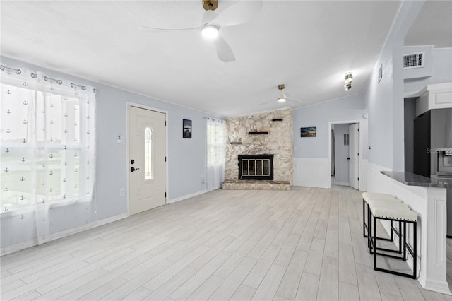 unfurnished living room featuring a stone fireplace, light wood-type flooring, ceiling fan, and vaulted ceiling