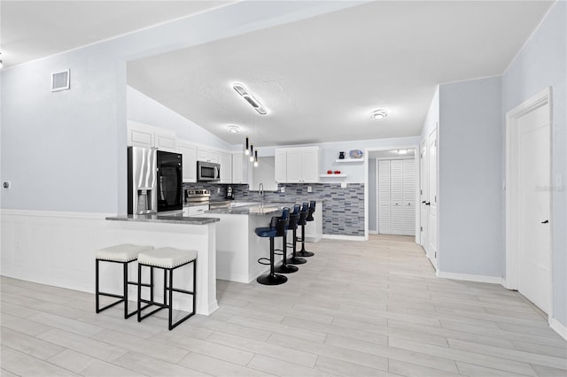 kitchen with kitchen peninsula, tasteful backsplash, a breakfast bar, white cabinets, and appliances with stainless steel finishes