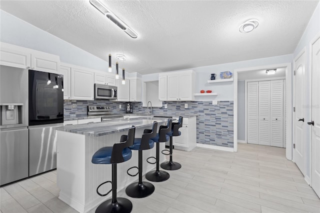 kitchen featuring tasteful backsplash, white cabinets, a kitchen island, and appliances with stainless steel finishes