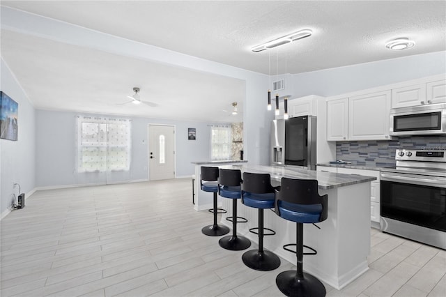 kitchen featuring a center island, white cabinetry, appliances with stainless steel finishes, backsplash, and ceiling fan