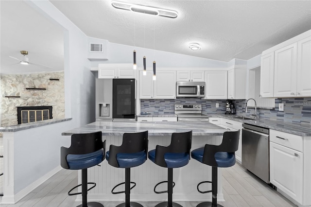 kitchen featuring a stone fireplace, white cabinetry, lofted ceiling, and stainless steel appliances