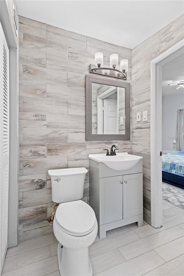 bathroom with tile floors, vanity, toilet, and tile walls