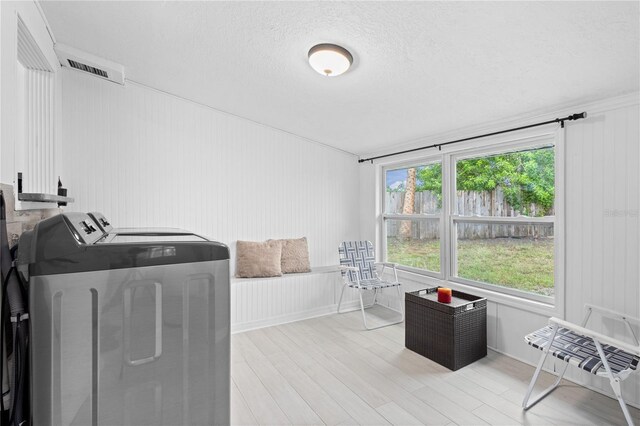 clothes washing area with light hardwood / wood-style floors, a textured ceiling, and washing machine and dryer