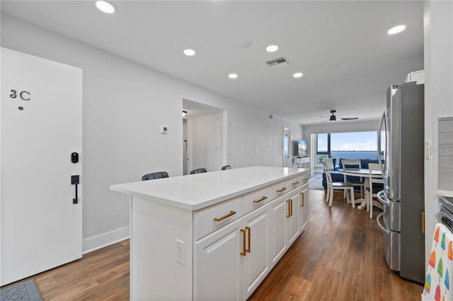 kitchen with white cabinetry, a center island, hardwood / wood-style floors, ceiling fan, and stainless steel refrigerator