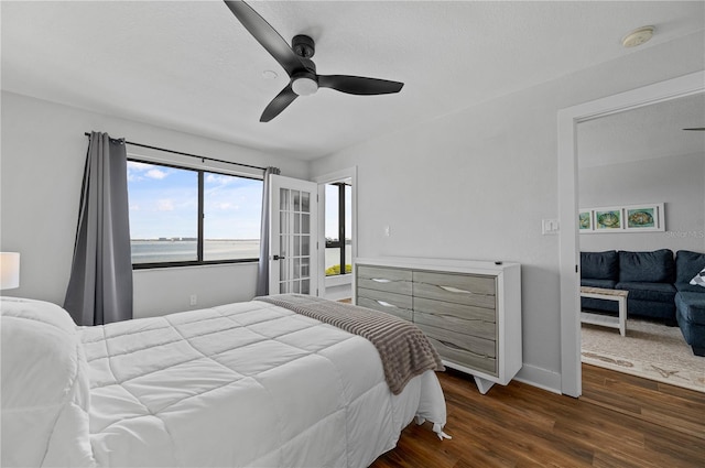 bedroom with dark wood-type flooring, ceiling fan, and a water view