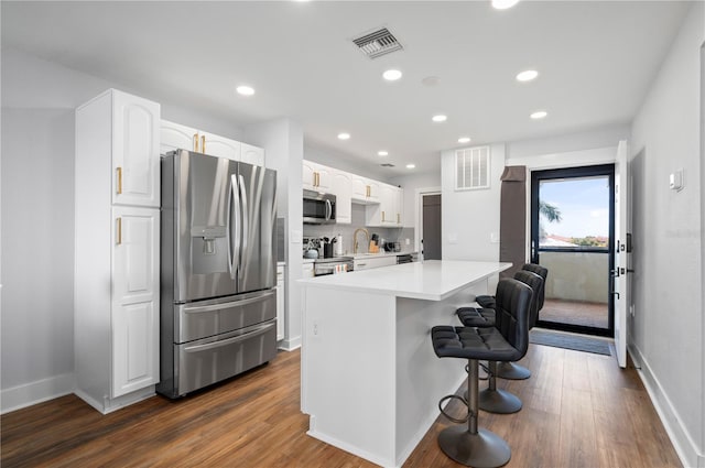 kitchen with a breakfast bar, dark hardwood / wood-style flooring, a kitchen island, appliances with stainless steel finishes, and white cabinets