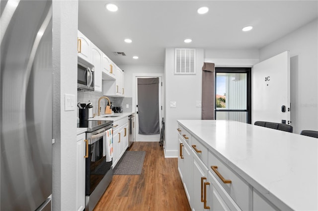 kitchen featuring stainless steel appliances, decorative backsplash, hardwood / wood-style flooring, sink, and white cabinetry