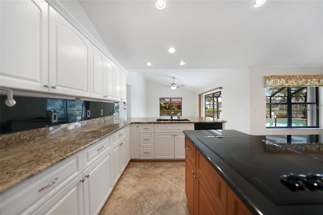 kitchen featuring vaulted ceiling, ceiling fan, sink, dark stone countertops, and white cabinets