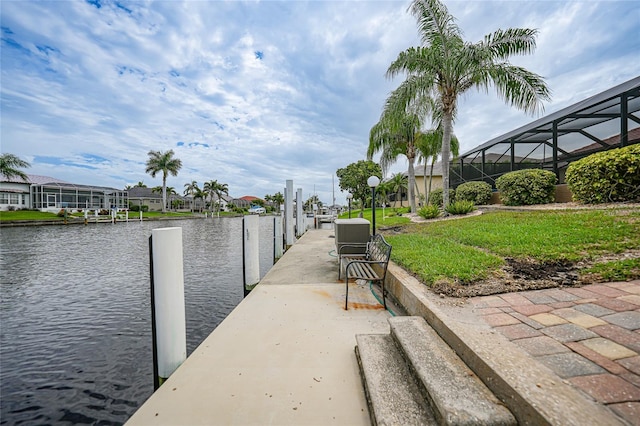 view of dock with a lanai, a water view, and a yard