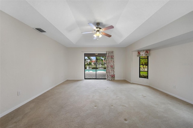 spare room featuring a raised ceiling, ceiling fan, and light carpet