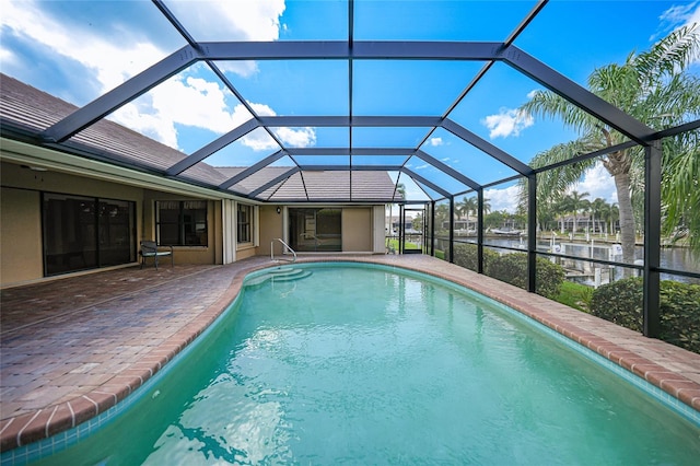 view of pool featuring glass enclosure, a water view, and a patio