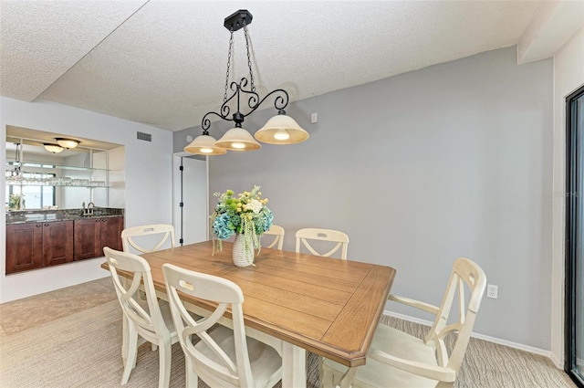 dining room with sink, light colored carpet, and a textured ceiling