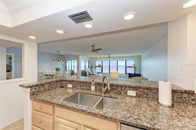 kitchen with light brown cabinetry, ornamental molding, dark stone counters, sink, and pendant lighting