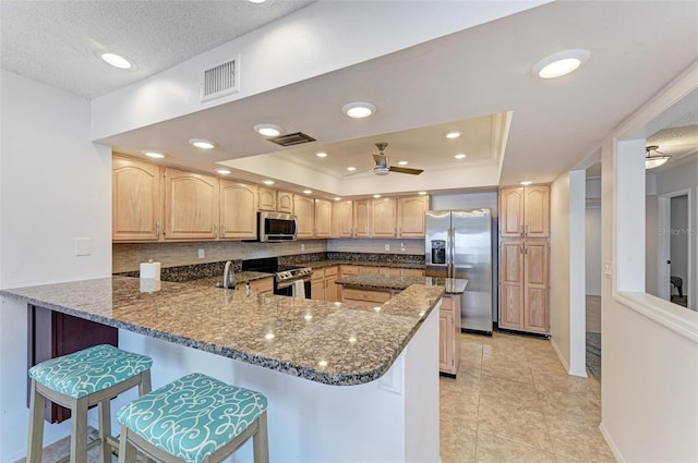 kitchen with a breakfast bar, a raised ceiling, kitchen peninsula, and appliances with stainless steel finishes