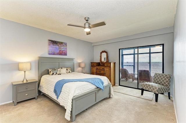 carpeted bedroom with access to exterior, ceiling fan, a water view, and a textured ceiling