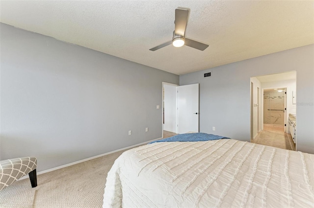 bedroom with a textured ceiling, connected bathroom, light colored carpet, and ceiling fan