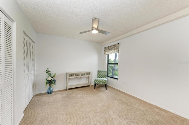 living area featuring ceiling fan, light colored carpet, and a textured ceiling