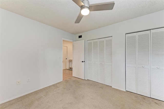 unfurnished bedroom with ceiling fan, light colored carpet, a textured ceiling, and multiple closets