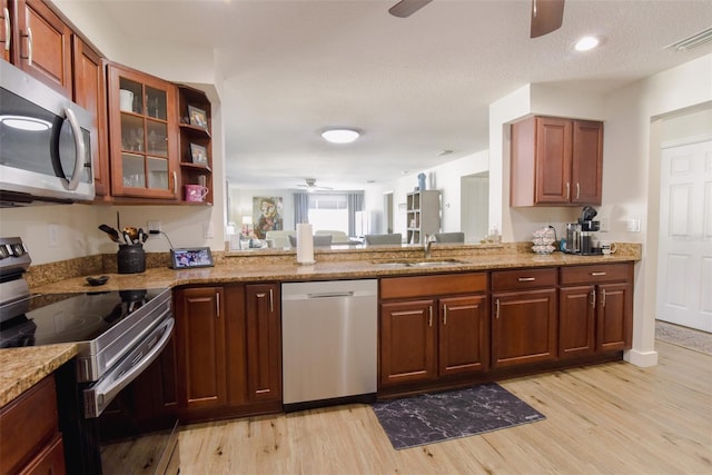 kitchen featuring sink, light stone counters, light hardwood / wood-style floors, a textured ceiling, and appliances with stainless steel finishes