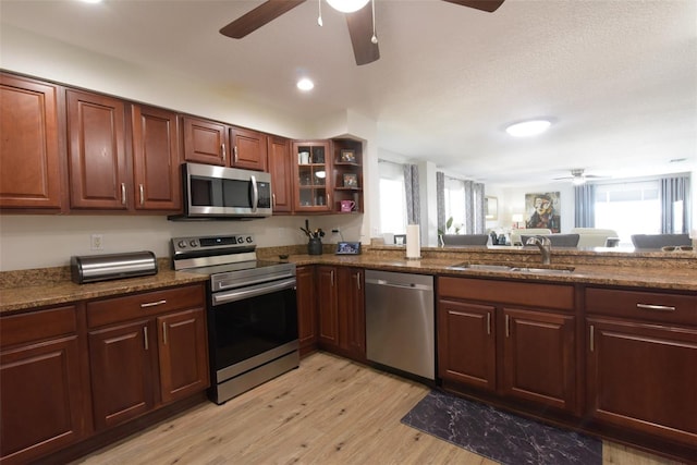 kitchen featuring appliances with stainless steel finishes, light hardwood / wood-style flooring, dark stone counters, and sink