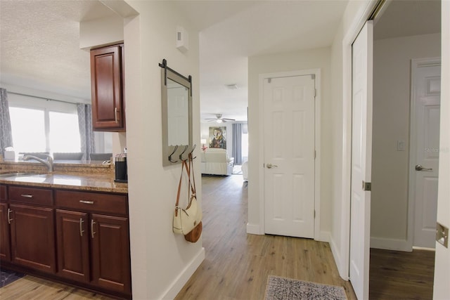 kitchen with sink, a barn door, light wood-type flooring, a textured ceiling, and stone countertops