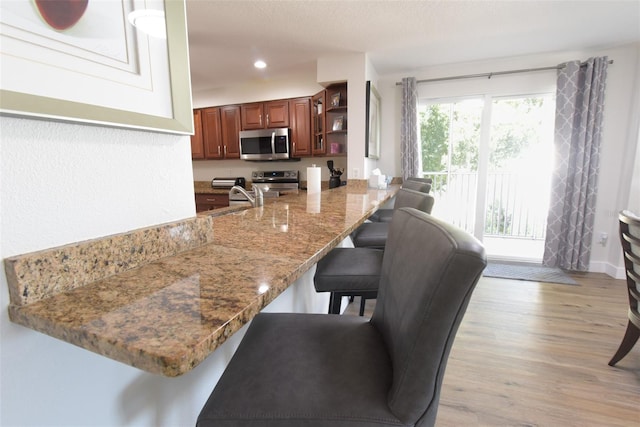 kitchen featuring stainless steel appliances, light stone counters, light hardwood / wood-style flooring, kitchen peninsula, and a breakfast bar