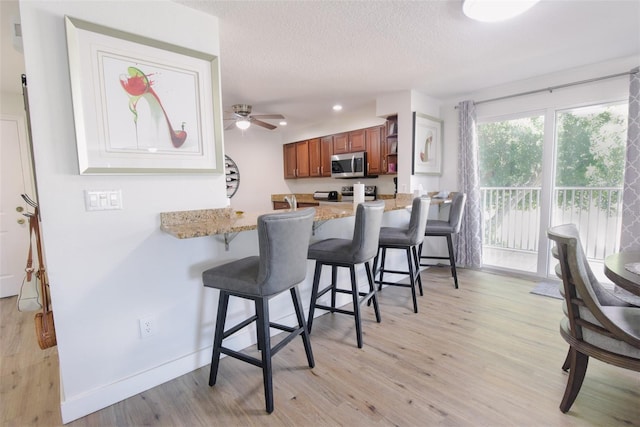 kitchen with kitchen peninsula, a kitchen breakfast bar, a textured ceiling, ceiling fan, and light hardwood / wood-style floors