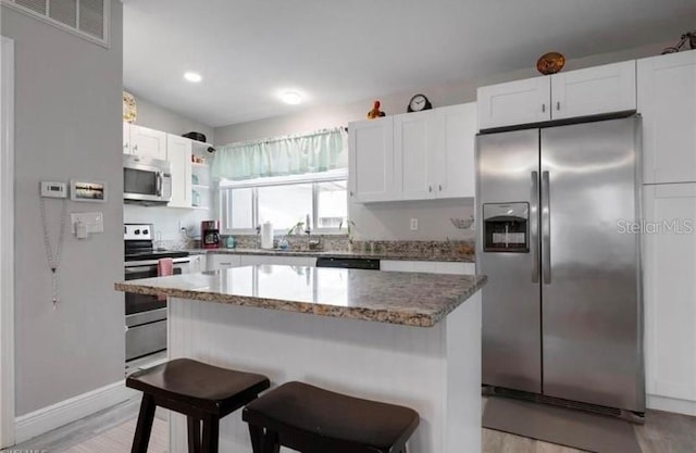 kitchen with white cabinetry, a kitchen island, stainless steel appliances, a kitchen bar, and dark stone counters