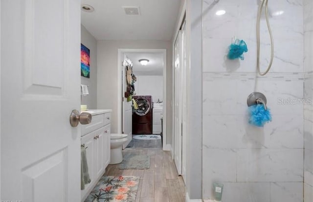 bathroom with toilet, independent washer and dryer, vanity, a tile shower, and hardwood / wood-style flooring