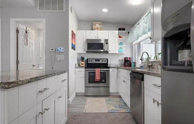 kitchen with dark stone countertops, white cabinetry, appliances with stainless steel finishes, lofted ceiling, and light hardwood / wood-style floors