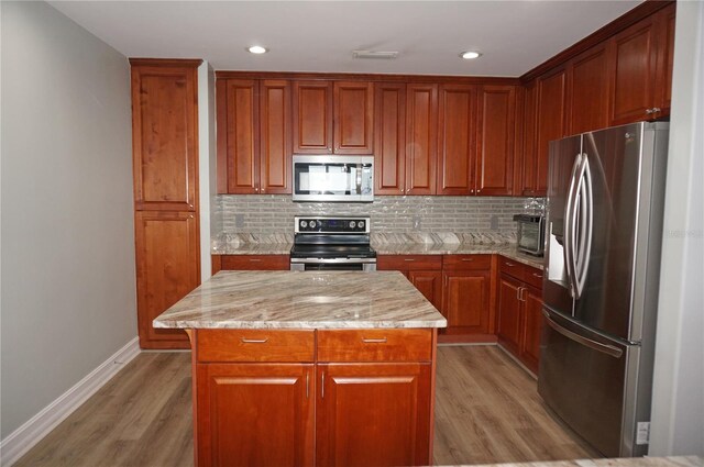 kitchen featuring a center island, stainless steel appliances, light stone counters, decorative backsplash, and light wood-type flooring