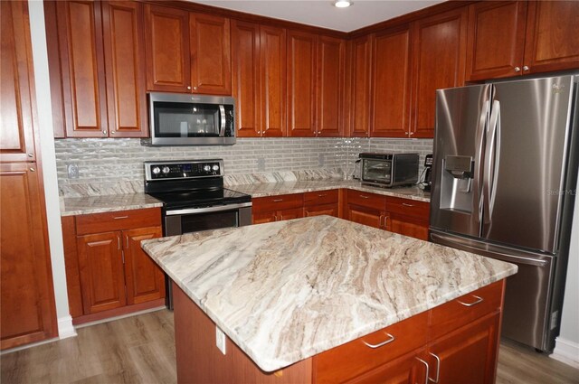 kitchen featuring light stone counters, a kitchen island, stainless steel appliances, and light wood-type flooring